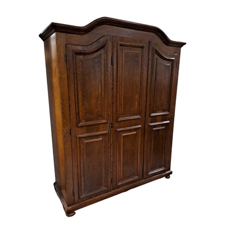 239 - AN OAK THREE DOOR WARDROBE the arched cornice above three panel doors containing hanging rails and s... 