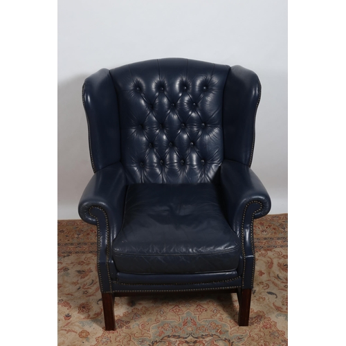 19 - A VINTAGE MAHOGANY AND HIDE UPHOLSTERED WING CHAIR with deep buttoned upholstered back and seat with... 