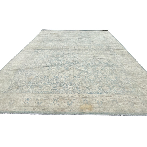 569 - A LARGE WOOL RUG the beige and light blue ground filled with stylised flowerheads and foliage 630cm ... 