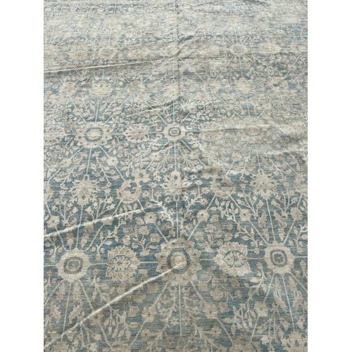 569 - A LARGE WOOL RUG the beige and light blue ground filled with stylised flowerheads and foliage 630cm ... 