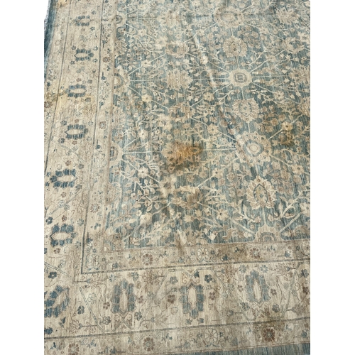 569 - A LARGE WOOL RUG the beige and light blue ground filled with stylised flowerheads and foliage 630cm ... 