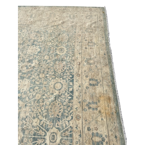 569 - A LARGE WOOL RUG the beige and light blue ground filled with stylised flowerheads and foliage 630cm ... 