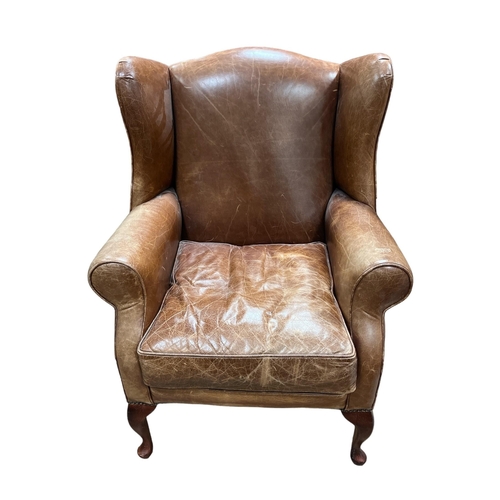 92 - A VINTAGE HIDE UPHOLSTERED WING CHAIR with scroll over arms and loose cushion on cabriole legs