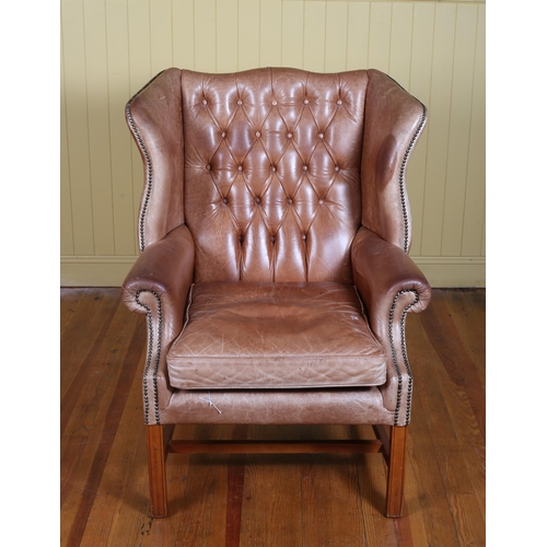 213 - A VINTAGE BROWN HIDE UPHOLSTERED WING CHAIR with deep buttoned upholstered back and seat with loose ... 