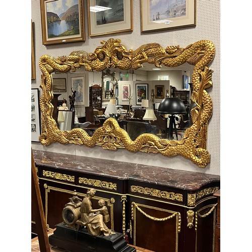 175 - A CONTINENTAL CARVED GILTWOOD MIRROR the shaped plate within a dragon frame 114cm (h) x 214cm (w)