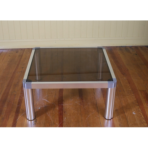 215 - A VINTAGE CHROME AND SMOKED GLASS COFFEE TABLE of rectangular outline with inverted angles on cylind... 