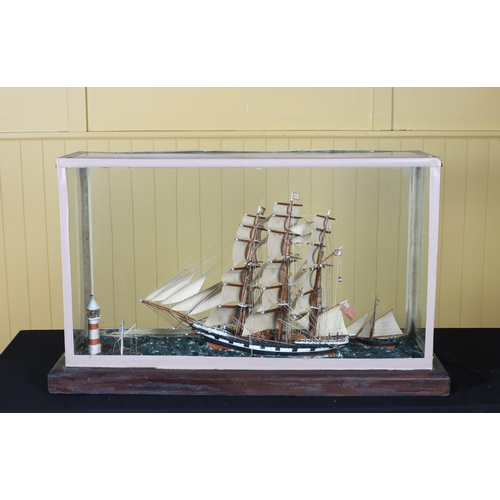 219 - A CASED MODEL OF A SAILING BOAT in a naturalistic setting with lighthouse in a  glazed case on hardw... 