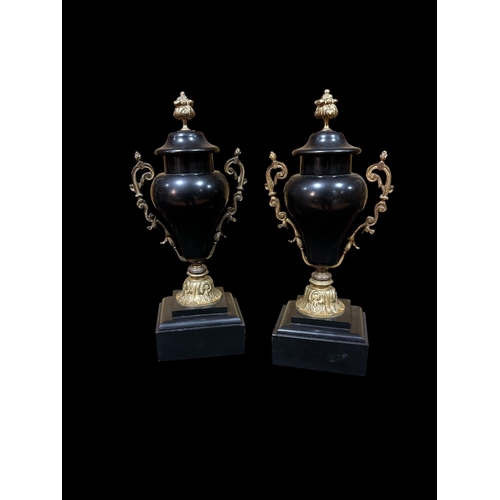 303 - A PAIR OF VINTAGE BLACK MARBLE AND GILT URNS with scroll handles raised on a rectangular stepped bas... 