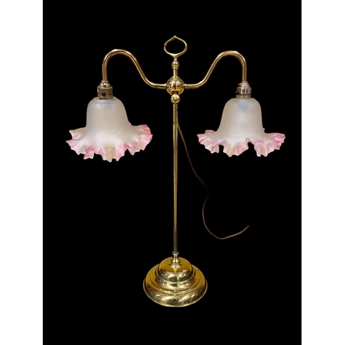 428 - A BRASS TWO BRANCH TABLE LAMP the scroll arms with frosted glass and pink shades raised on a circula... 