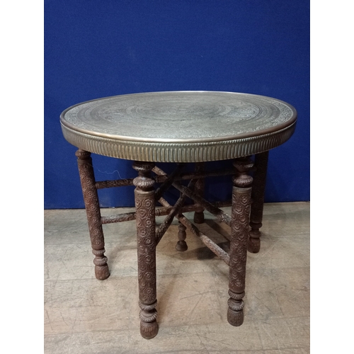 256 - A VINTAGE BRASS AND HARDWOOD TABLE the circular brass top raised on carved legs joined by cross stre... 