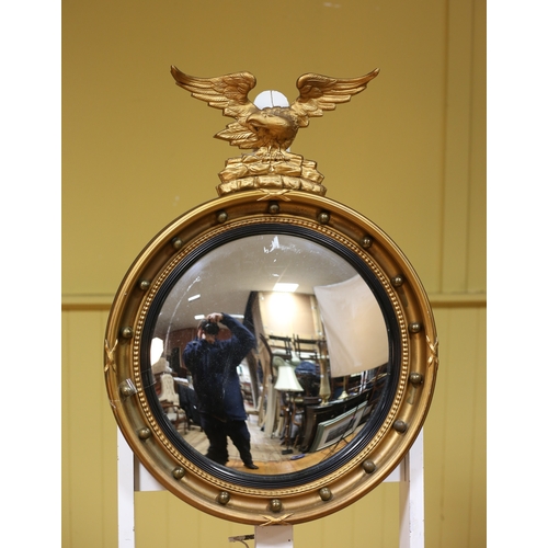 309 - A GILT FRAME CONVEX MIRROR the ball and strapwork frame surmounted by a winged eagle perched on a ro... 