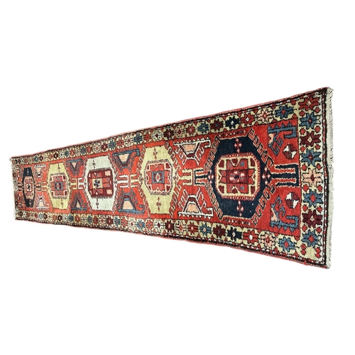 326 - A TURKISH WOOL RUNNER the light pink, indigo and beige ground with central panel filled with serrate... 