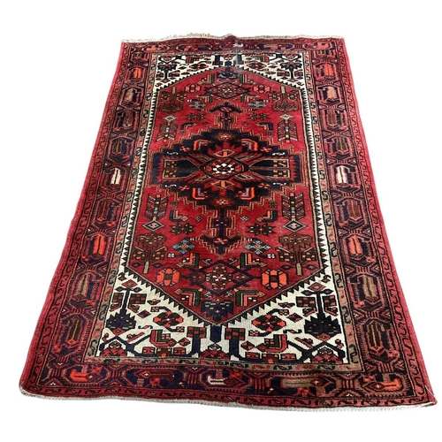 183 - AN ORIENTAL WOOL RUG the red, wine and indigo ground with central panel filled with serrated panels,... 