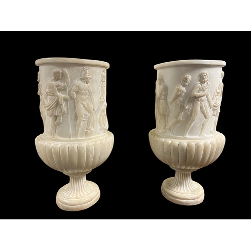 A PAIR OF COMPOSITION NEO CLASSICAL STYLE URNS each of cylindrical form moulded in relief with figures above a circular spreading foot 47cm (h) x 22cm (d)