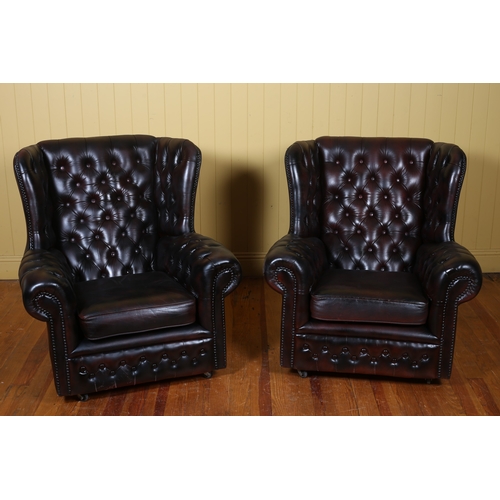 A PAIR OF HIDE UPHOLSTERED WING BACK LIBRARY CHAIRS each with a deep buttoned upholstered back with loose cushion and scroll over arms on castors