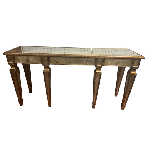A THEODORE ALEXANDER GILT AND GLAZED CONSOLE TABLE of rectangular outline the shaped top with glazed inset above three frieze drawers on square tapering legs with mirror inset 93cm (h) x 51cm (w) x 184cm (d)
