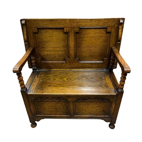 A GOTHIC STYLE OAK MONK'S BENCH the hinged top with shaped arms and bobbin turned supports with hinged compartment and panelled frieze on bun feet 94cm (h) x 91cm (w) x 46cm (d)