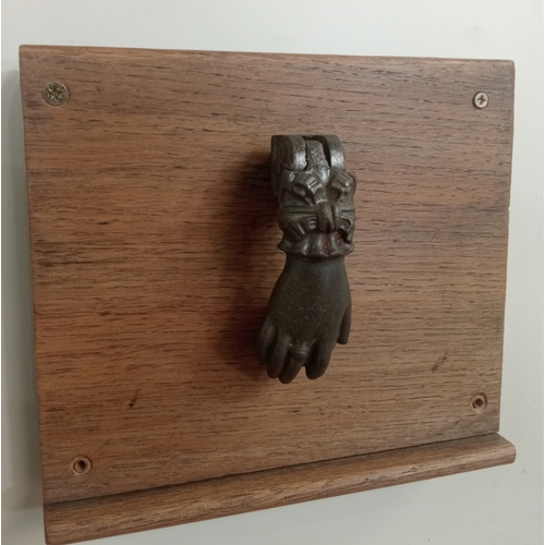 617 - A CAST IRON DOOR KNOCKER in the form of a hand raised on a hardwood plaque 21cm (h) x 24cm (w)