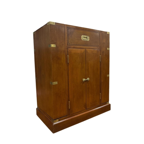 AN ART DECO STYLE CHERRYWOOD AND BRASS BOUND CAMPAIGN STYLE DRINKS CABINET of rectangular outline the shaped top with frieze drawer and cupboards flanked on each side by hinged cupboards on platform base 88cm (h) x 70cm (w) x 41cm (d)