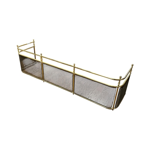 205 - A VINTAGE BRASS AND WIRE MESH FIREPLACE FENDER featuring hexagonal finials and bobbin turned baluste... 