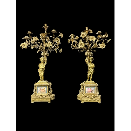 A FINE PAIR OF 19TH CENTURY FRENCH GILT BRONZE, COPPER AND PORCELAIN FIVE LIGHT FIGURAL CANDELABRA each depicting a putto holding aloft a cornucopia issuing flowering branches and candle sconces the figure stood atop garlanded and relief cast architectural bases fitted with hand painted porcelain panels stood on gadrooned circular feet approx. 84cm (h) x 46cm (w) x 23cm (d) (2)