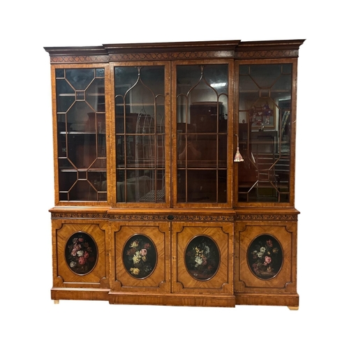 A VERY FINE AND IMPRESSIVE SATINWOOD AND PAINTED LIBRARY BOOKCASE of breakfront outline the moulded cornice above four astragal glazed doors containing adjustable shelves the base with cupboards centred by oval painted floral panels on platform support 238cm (h) x 234cm (w) x 52cm (d)