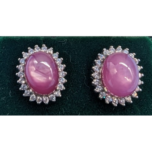 412 - A pair of silver studs set with cabochon ruby surrounded by a halo of white round cubic zirconia sto... 