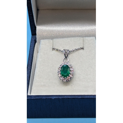 762 - 18ct white gold oval emerald and diamond cluster pendant on a silver chain.  Emerald 0.83ct.  Diamon... 