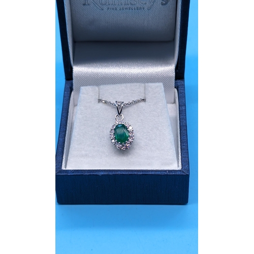 762 - 18ct white gold oval emerald and diamond cluster pendant on a silver chain.  Emerald 0.83ct.  Diamon... 