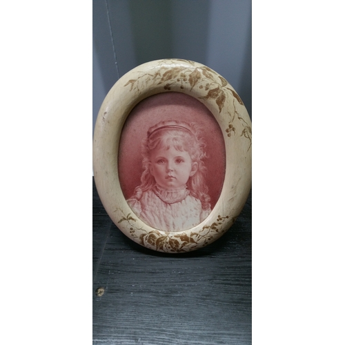 1277 - An Oval Wooden Framed Ceramic Picture Of A Child.  38cm High, 28cm Wide.