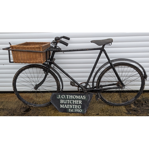 Vintage Tradesman&rsquo;s Butcher&rsquo;s Delivery Bicycle with Basket

A vintage tradesman&rsquo;s delivery bicycle, formerly used by J.O. Thomas, Butcher, Maesteg (Est. 1910), complete with large wicker front basket and period painted shop sign panel.

The bicycle of traditional gents&rsquo; frame with rear carrier, front-mounted metal basket frame housing a wicker basket, and leather saddle (marked &ldquo;Dunlop&rdquo;). Finished in black with visible age-related wear throughout. The painted wooden shop advertising board is included with the lot.

Showing surface rust, paint loss, wear to tyres and chain, and general age-related condition consistent with long-term storage. Restoration required. Untested and sold as a display/restoration piece.

A characterful example of a vintage commercial delivery bicycle with strong decorative and display appeal.