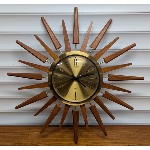 Anstey Wilson Teak and Brass Sunburst Wall Clock

A mid-century style teak and brass sunburst wall clock by Anstey Wilson, England, the circular brushed brass dial with baton hour markers and black hands, signed to the centre and marked Quartz, within a brass bezel and radiating teak spokes.

Quartz battery movement.

Diameter: approx. 48 cm

Condition: general light wear; minor marks to spokes and bezel consistent with age; movement untested.