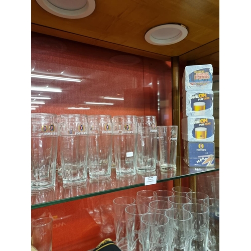 184 - 12 x fosters lager pint glasses with 3 half pint glasses and 4 x full packs of beer mats