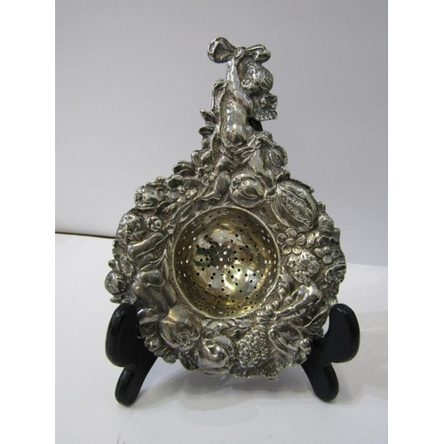 182 - SILVER TEA STRAINER, ornate tea strainer with cupid finial and fruit decoration in relief to the out... 