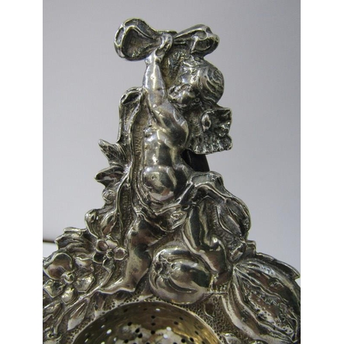 182 - SILVER TEA STRAINER, ornate tea strainer with cupid finial and fruit decoration in relief to the out... 