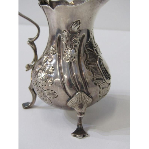 250 - GEORGE III SILVER EMBOSSED CREAM JUG, on tripod feet, London possibly 1763, 91 grams