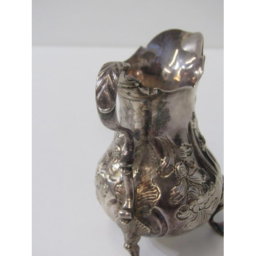 250 - GEORGE III SILVER EMBOSSED CREAM JUG, on tripod feet, London possibly 1763, 91 grams