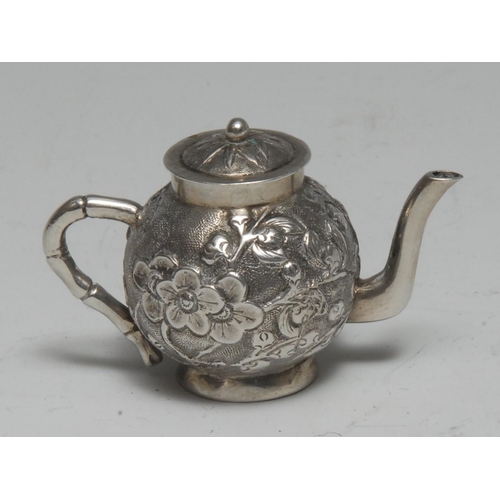 1005 - A Chinese silver miniature teapot, chased with blossoming prunus, faux bamboo handle, 4.5cm long