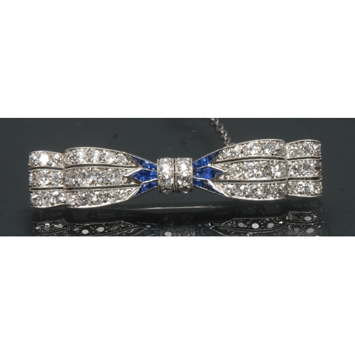 1128 - An Art Deco diamond and sapphire tied bow brooch, central ridge of eight round brilliant cut diamond... 