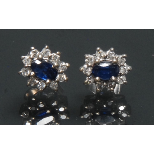 1131 - A pair of sapphire and diamond cluster earrings, each with a central oval blue sapphire surrounded b... 