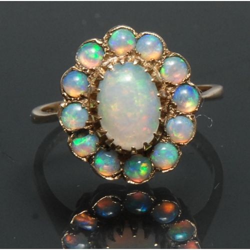 1134 - An opal cluster ring, central oval opal cabochon surrounded by a collar of twelve similar round cabo... 