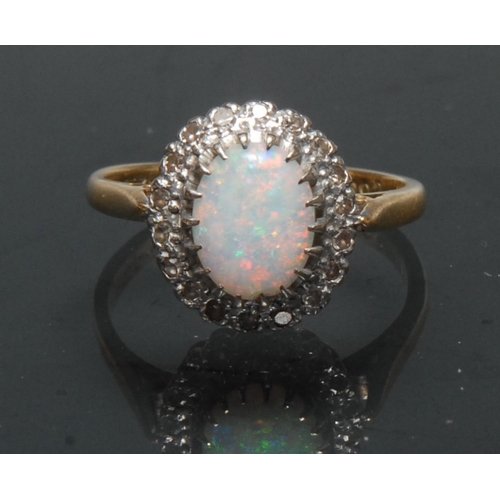 1140 - A diamond and opal cluster ring, central oval opal cabochon flashing vibrant red, green, blue and vi... 