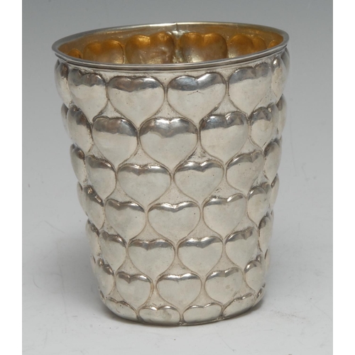 913 - A German silver tapered cylindrical beaker, profusely chased with rows of heart motifs, gilt interio... 