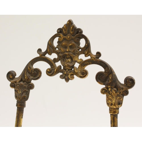 3042 - A 19th century gilt metal table-top easel, in the Baroque taste, crested by a foliate mask, leafy sc... 