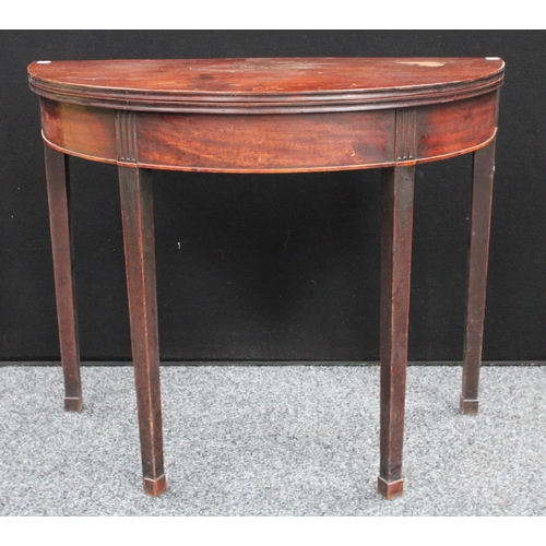 58 - A George III mahogany demilune tea table, folding top with concave edge above a deep frieze, tapered... 