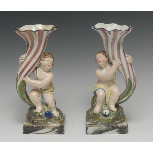 25 - A pair of Staffordshire figural spill vases, of cherubs holding cornucopias, lightly coloured in pin... 