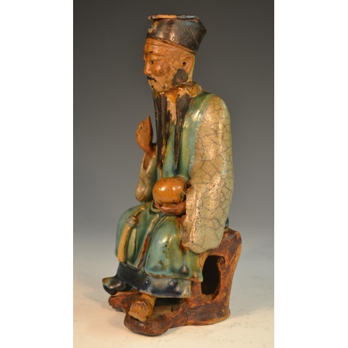 301 - A Chinese stoneware figure, of an immortal, seated, holding a peach, glazed in mottled tones of gree... 