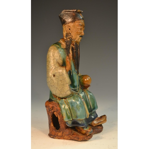 301 - A Chinese stoneware figure, of an immortal, seated, holding a peach, glazed in mottled tones of gree... 