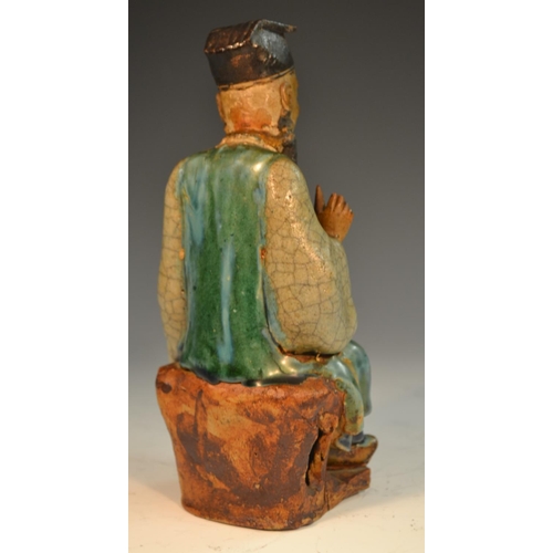 301 - A Chinese stoneware figure, of an immortal, seated, holding a peach, glazed in mottled tones of gree... 