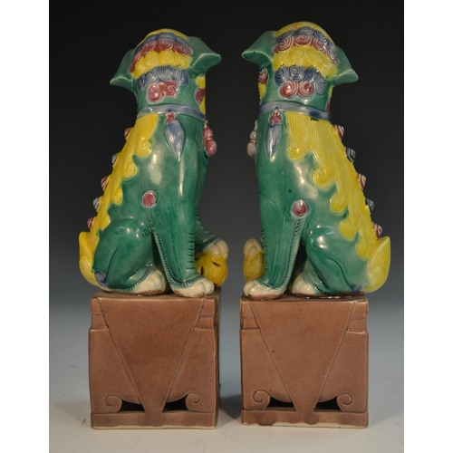 321 - A pair of Chinese temple lions, modelled as male and female seated to left and right, glazed in tone... 